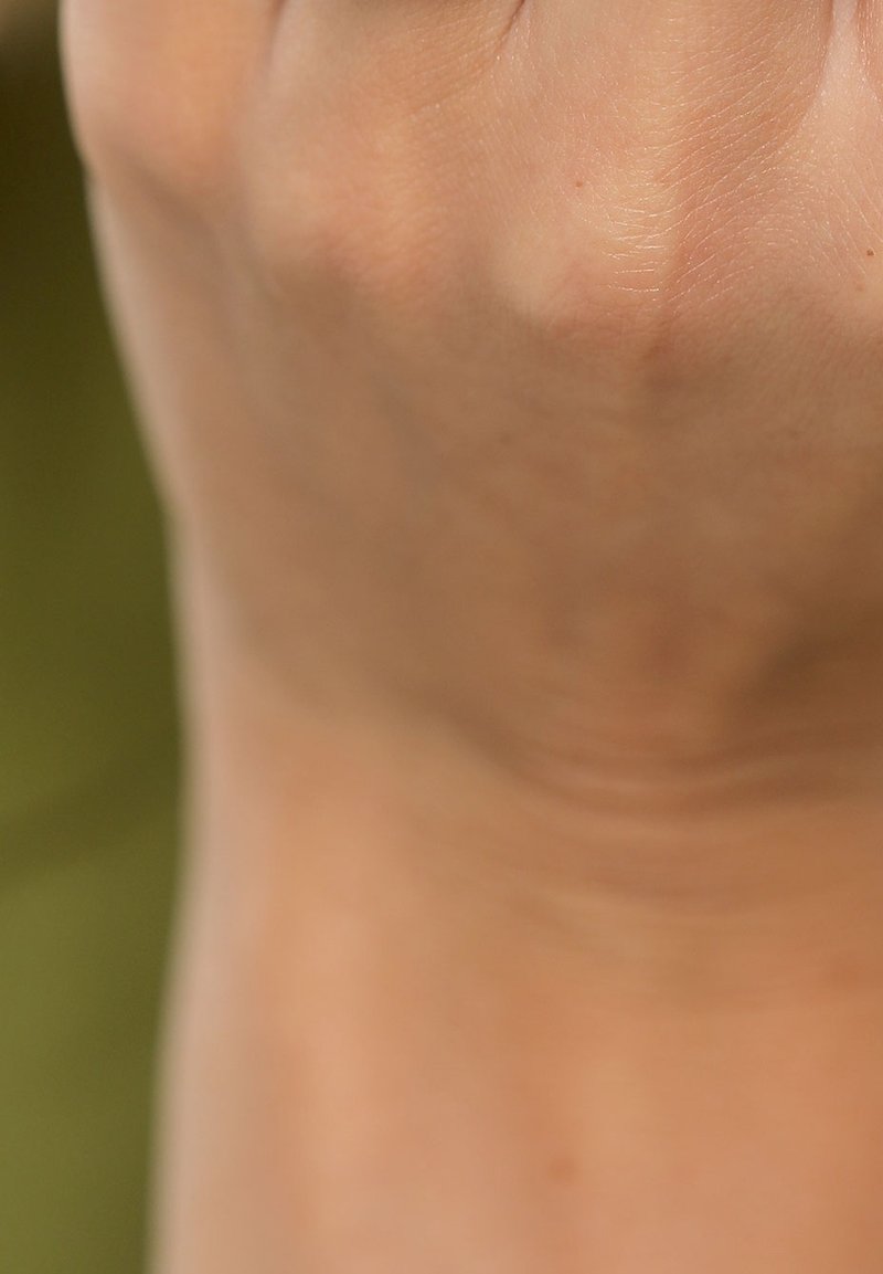 Gros plan sur un poing serré montrant la texture de la peau et les veines sur un fond vert flou.
