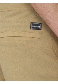 Beżowe szorty Volcom o gładkiej, teksturowanej tkaninie. Zawierają tylną kieszeń z dekoracyjnym przeszyciem oraz czarną naszywką z logo.