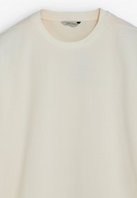 Sudadera beige claro con cuello redondo, textura suave y diseño minimalista. Sin patrones visibles ni detalles metálicos.