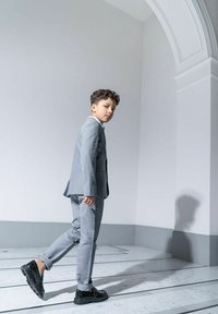 Szary garnitur o dopasowanym kroju, z wyraźną strukturą, zestawiony z czarnymi butami. Gładka tekstura, klasyczny kołnierz i dopasowana sylwetka.