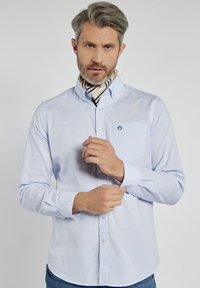 Jasnoniebieska koszula z guzikami i kieszonką, wykonana z gładkiego materiału; posiada małe logo oraz kołnierzyk w szpic. Akcent z fakturowanym szalikiem.