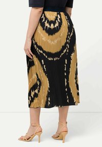 Plisserad midiklänning i ett svart och tan-mönster, med ett åtsittande midjeband och en slät textur, kombinerad med nude högklackade sandaler med remmar.