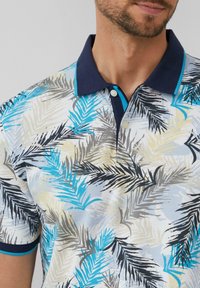 Krótki rękaw polo w jasnoniebieskim kolorze z wzorem liści palmowych w odcieniach teal, czerni i beżu. Granatowy kołnierz z kontrastującymi akcentami turkusowymi.