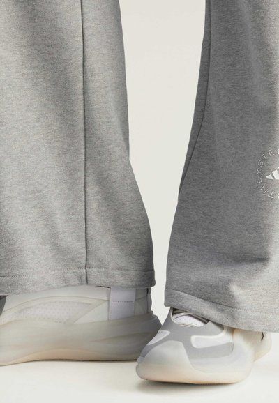 Sivé tepláky s hladkým povrchom, s bočným švom a logom. V páre so svetlosivými športovými topánkami so štýlovým dizajnom.