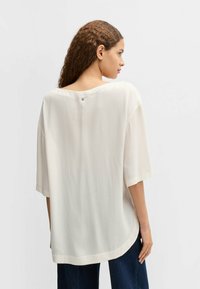 Blusa leggera e morbida di colore avorio, con scollatura rotonda, maniche corte e un dettaglio con bottoni sul retro.