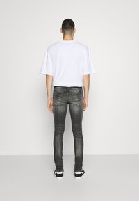 Jeans de mezclilla gris ajustados con un ligero desgaste, cinco bolsillos y costuras cosidas, combinados con una camiseta blanca holgada y zapatillas negras.