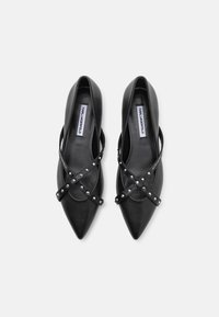 Ballerines noires à bout pointu avec une tige en cuir lisse, des sangles croisées avec des clous argentés, et un design épuré. Étiquette intérieure visible.
