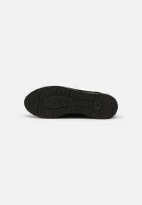 Semelle de chaussure noire avec motif de bande de roulement texturé comprenant des formes en chevrons et circulaires sur un fond blanc uni.