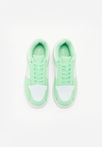 Sneaker verde chiaro con accenti bianchi, caratterizzati da una tomaia testurizzata, punta tonda, dettagli perforati e lacci piatti.