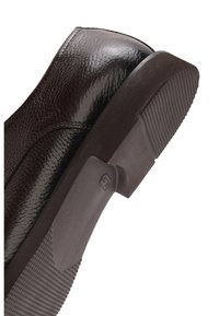 Close-up van een bruine leren schoen met textuur, de hiel en zool met een profielpatroon en een klein geëmbossed logo op de rubberen zool.