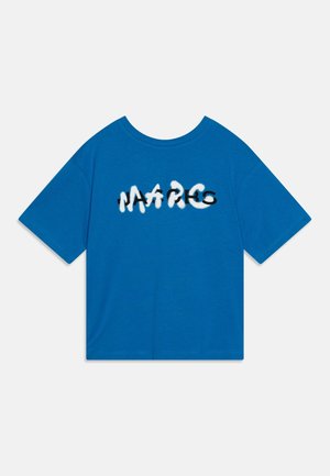 Niebieski t-shirt z krótkim rękawem z zniekształconym czarno-białym napisem „NAPAS” na piersi na jednolitym szarym tle.