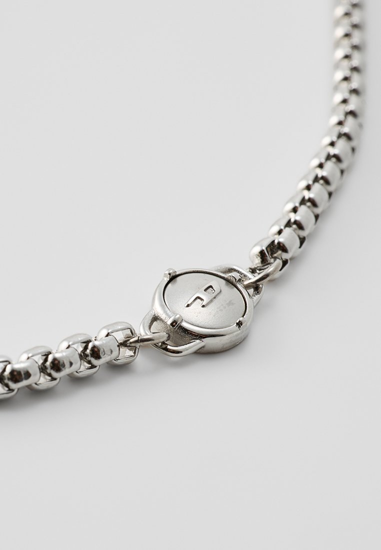 Collier en chaîne argentée comportant des maillons ronds et ovales avec un fermoir circulaire. Le fermoir arbore une lettre "P" en relief sur sa surface.