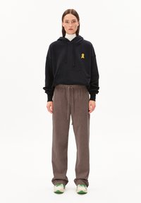 Haut à capuche noir avec un logo en ruban jaune, assorti à un pantalon en velours côtelé marron avec une taille à cordon. Baskets blanches avec des accents verts.