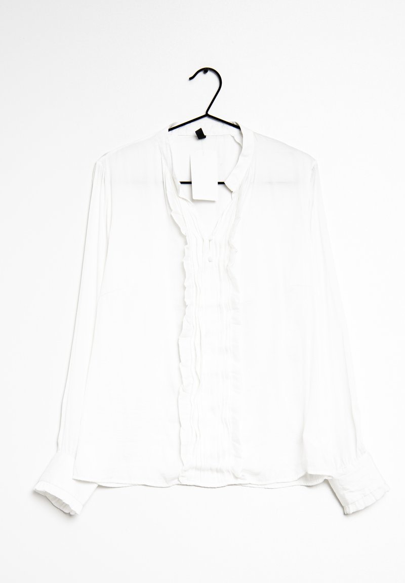 White long-sleeve blouse made of lightweight fabric, featuring a ruffled front placket, button closure, and a hanging tag attached.