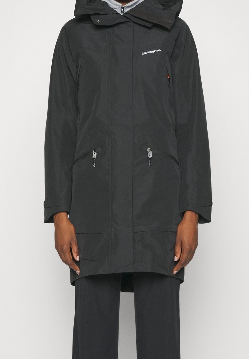 Cappotto impermeabile nero con cappuccio, cerniere sulle tasche frontali e tessuto testurizzato. Presenta una vestibilità comoda e maniche lunghe.