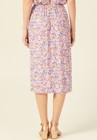 Blumenmidi-Dress mit einem pinken Hintergrund und bunten Mustern. Gummibund und ein Schlüsselverschluss-Detail auf der Rückseite. Ein Paar goldene Absätze.