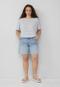 Gestreepte, lichtblauwe blouse met korte mouwen, gecombineerd met mid-blauwe denim shorts met rafelige zomen, aangevuld met witte sandalen met banden.