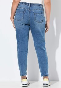 Jean en denim bleu avec une coupe fuselée et une taille élastique, dotée de deux poches arrière et de poignets retroussés, associée à des baskets multicolores.