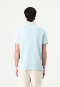 Polo de color azul claro hecho de algodón, con un cuello corto, mangas cortas y un dobladillo recto. Textura suave con sutiles detalles de costura.