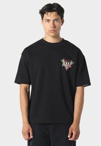 Musta lyhythihainen t-paita pyöreällä kaula-aukolla, jossa on värikäs brodeerattu logo rinnassa. Valmistettu puuvillasta, rento malli.