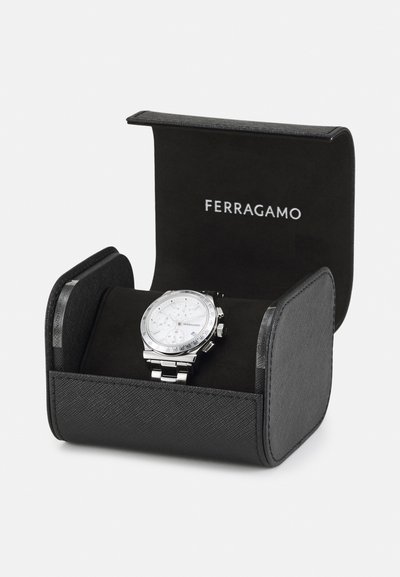 Silver watch with a white dial, chronograph features, and a polished band displayed in a black fabric-covered case with Ferragamo branding.