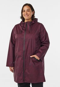 Impermeable abrigo de lluvia color marrón burdeos con un patrón de hojas negras, que cuenta con capucha, cierre de cremallera, bolsillos laterales y cordones ajustables.