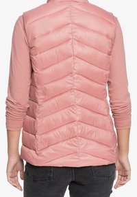 Roze puffer-vest met chevron-stiksels, een hoge kraag en een lichtgewicht, glanzende afwerking. Draagt over een top met lange mouwen en een spijkerbroek.