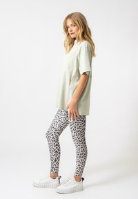 Mentolově zelené oversized tričko, legíny s šedobílým leopardím vzorem a bílé platformové tenisky s texturovanou podrážkou.