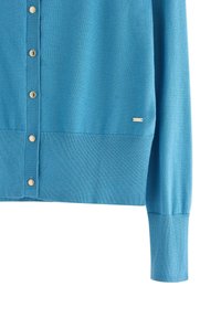 Cardigan azzurro chiaro realizzato in tessuto morbido, caratterizzato da una chiusura a bottoni con bottoni metallici e polsini e orlo a coste. Presenza di un piccolo logo decorativo.