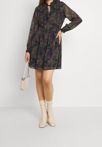 Blommönstrad klänning med volangkrage, långa ärmar och utsvängd kjol, tillsammans med beige knähöga stövlar och en liten handväska.