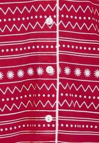 Crvena tkanina košulja s bijelim geometrijskim uzorcima, horizontalnim linijama i dugmadima. Uzorci uključuju cik-cak, točkice i zvjezdaste oblike.