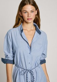 Camicia a righe blu e bianche con colletto abbottonato, maniche arrotolate con un accento a motivo e vita con coulisse.