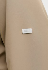 Bežna tkanina z teksturirano površino, ki ima pravokotni srebrni napis s hot stampanjem "JACK&JONES PREMIUM." Minimalističen dizajn in mehak material.