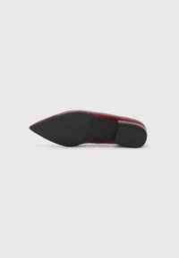 Chaussure à talon haut en cuir verni rouge avec un bout pointu et une semelle en caoutchouc noir texturé, présentant une finition lisse et brillante.
