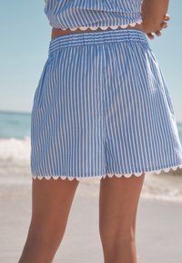 Sinivalkoraidalliset shortsit aaltoilevalla helmalla, joissa kevyt kangas ja joustava vyötärönauha mukavuutta varten.