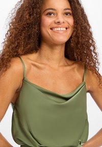 Camisole en satin vert olive avec bretelles fines, présentant un col drapé et une texture lisse, mettant en valeur son design doux et fluide.