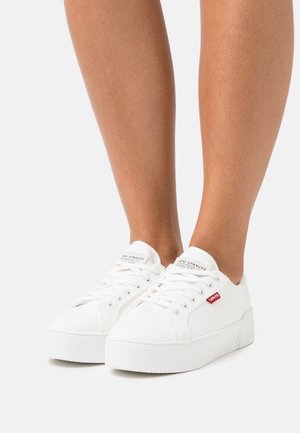 Baskets en toile blanche avec une finition texturée, dotées d'un bout rond, d'un système de laçage, de semelles blanches et d'un accent du logo Levi's rouge.