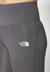 Szürke, magas derekú leggings rugalmas anyagból, amelyen az "The North Face" kis fehér logója található a bal alsó oldalon.