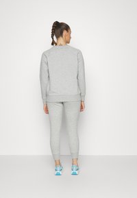 Sudadera gris ajustada y leggings, hechos de un material suave. Textura sutil con puños acanalados. Complementados con zapatillas deportivas azul claro.