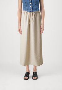 Denim ærmeløs top med knapper, parret med en beige, ankel-lang nederdel med elastisk talje og snøre, båret med sorte slidesandaler.
