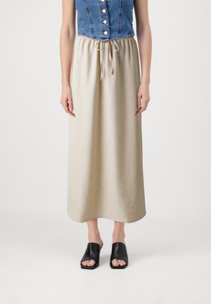 Denim ærmeløs top med knapper, parret med en beige, ankel-lang nederdel med elastisk talje og snøre, båret med sorte slidesandaler.