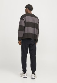 Katoenen pullover met horizontale strepen in zwart en grijs, relaxed fit, gecombineerd met slim-fit zwarte joggingbroeken en lichtgrijze sneakers.