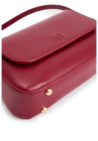 Rode leren crossbody tas met een gladde afwerking, klep sluiting, gouden hardware-accenten en ronde studs aan de basis. Compact rechthoekige vorm.