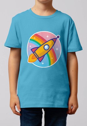 Kind trägt blaues T-Shirt mit einer gelben Rakete, die über einem Regenbogen und Sternen startet, auf der Vorderseite.