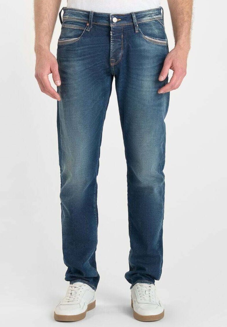 Vaqueros de mezclilla azul con un corte recto, ligero desgaste, diseño de cinco bolsillos y costuras en contraste, combinados con zapatillas blancas.