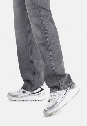 Baskets de sport blanches et grises avec une tige en mesh texturé, semelle épaisse et une marque bien visible. Portées avec un jean gris ample.