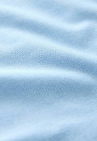 Tissu bleu clair doux avec une texture tissée fine et régulièrement espacée, présentant de légers plis créant des ombres et des reflets subtils.
