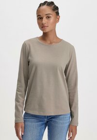 Langärmliges, helles Taupe-Hemd aus weichem Stoff, mit rundem Halsausschnitt und lockerer Passform, kombiniert mit blauen Jeans.