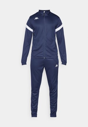 Survêtement marine en matériau lisse, composé d'une veste zippée avec des rayures blanches et d'un pantalon avec des poignets élastiques et un détail de logo.
