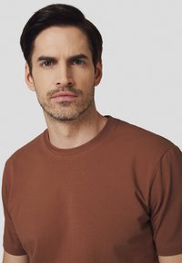 Brązowa, krótkim rękawem koszulka T-shirt wykonana z miękkiego materiału bawełnianego, z klasycznym okrągłym dekoltem i gładką fakturą.